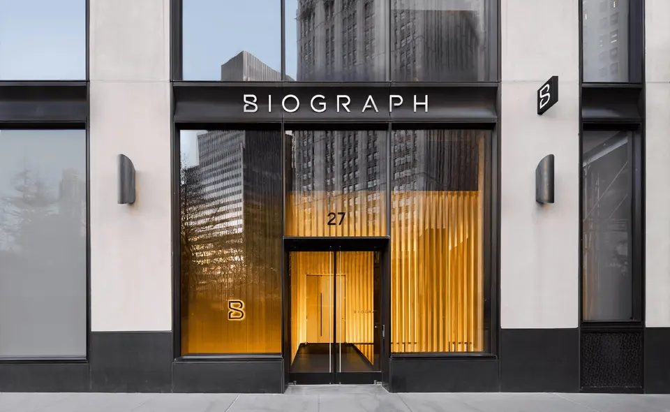 Biograph storefront at 27 Park Row with glowing wood-slat interior behind glass