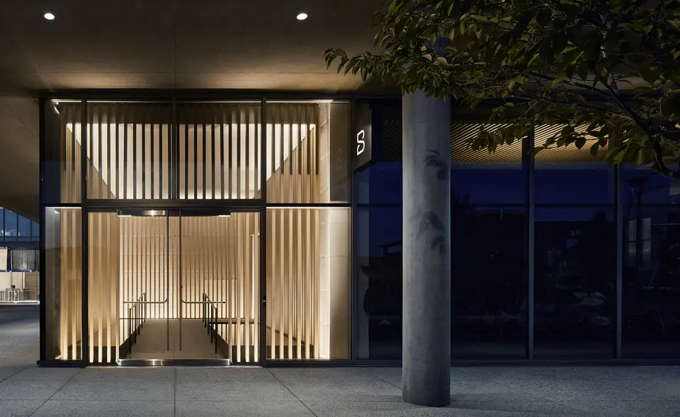 Glass entrance with lit wood-slat lobby at Biograph San Francisco Bay Area at dusk