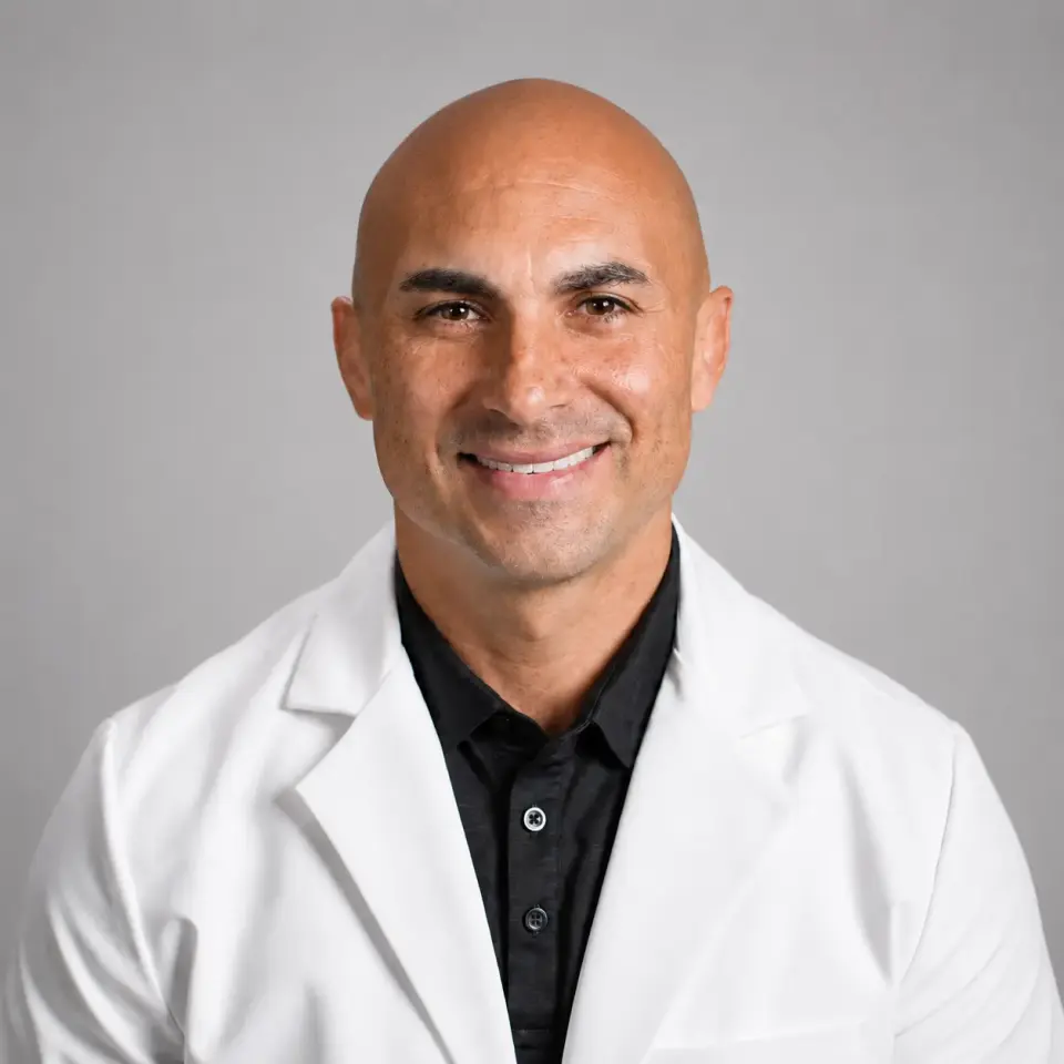 Portrait of Dr. Cas Santana of Cenegenics Dallas in a white coat over a black shirt