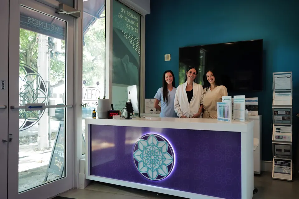 Three staff members behind the purple Centner reception desk at Centner Wellness Coral Gables