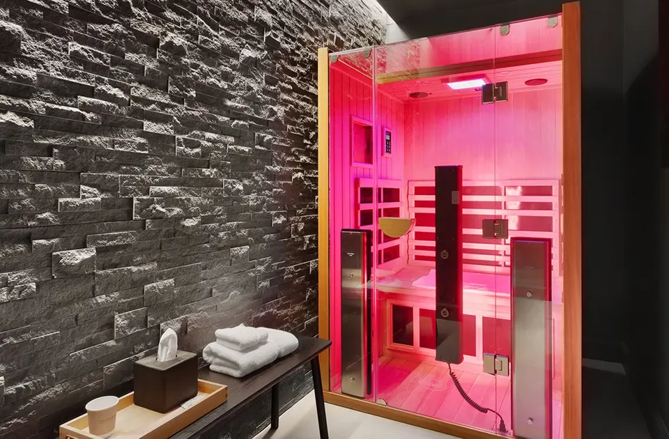 Infrared sauna cabin glowing pink beside a stone wall and bench at Clean Market FiDi