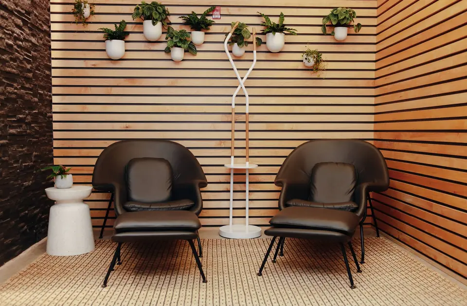 Two lounge chairs against a wood-slat wall with hanging plants at Clean Market Midtown East