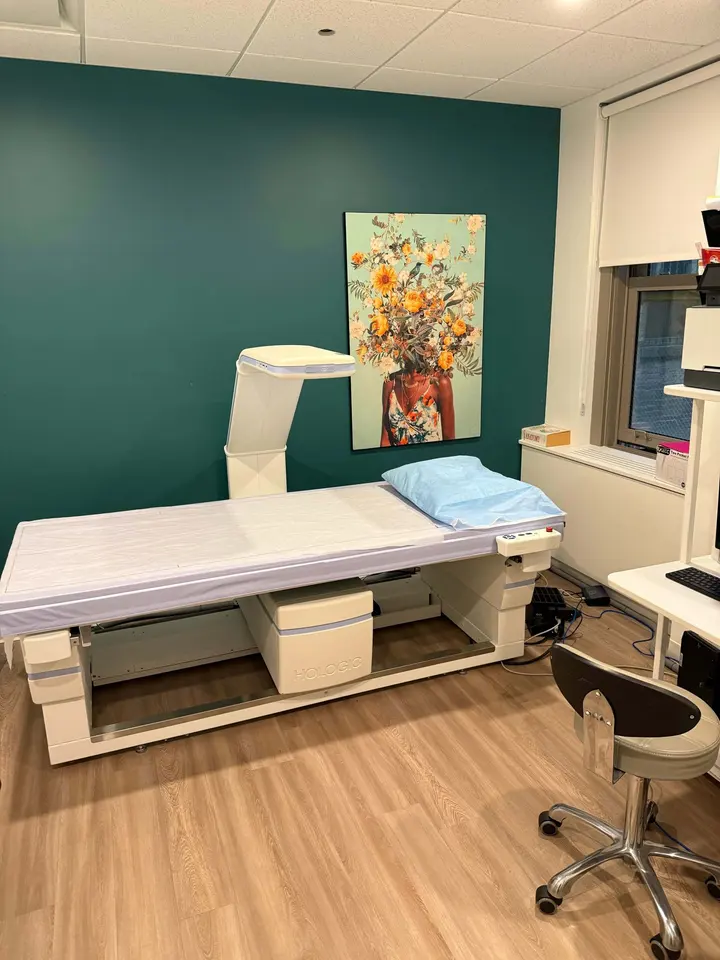 DEXA scanner table in a treatment room with a teal accent wall and floral artwork at Dexaslim
