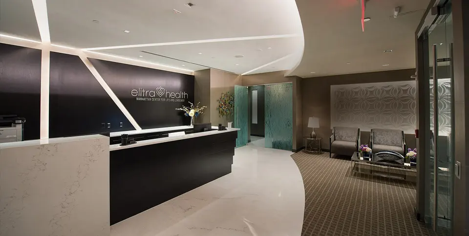 Reception desk and waiting lounge with curved light-strip ceiling at Elitra Health