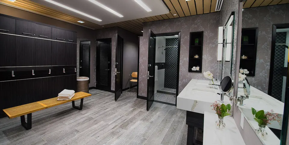 Locker room with dark wood lockers, bench and vanity at Elitra Health