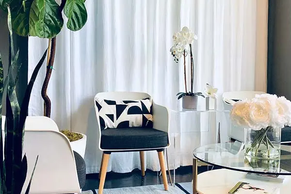 Lounge seating at EvolvE with black-and-white armchairs, a glass coffee table, white flowers and sheer curtains