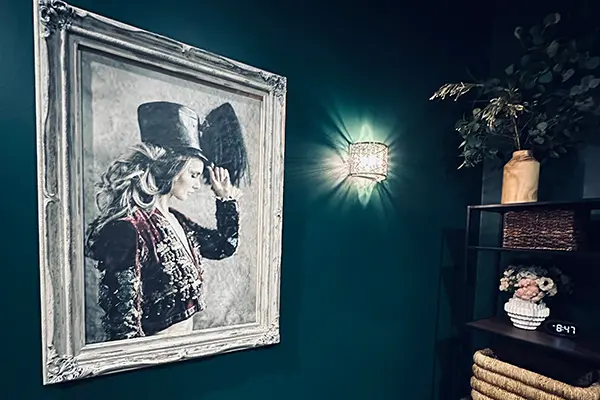 Corner of a teal-walled room at EvolvE with a large framed portrait, a wall sconce and a shelf of towels