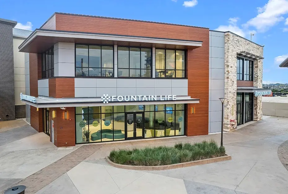 Two-story wood-and-stone building with Fountain Life signage above its glass storefront