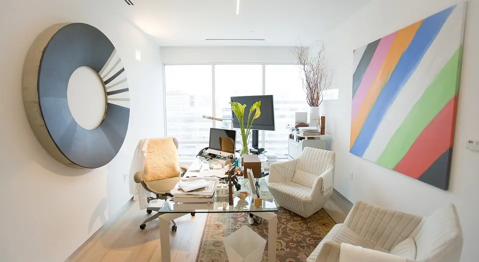Bright consultation office with glass desk, white armchairs and a large striped artwork at Hall Longevity Clinic