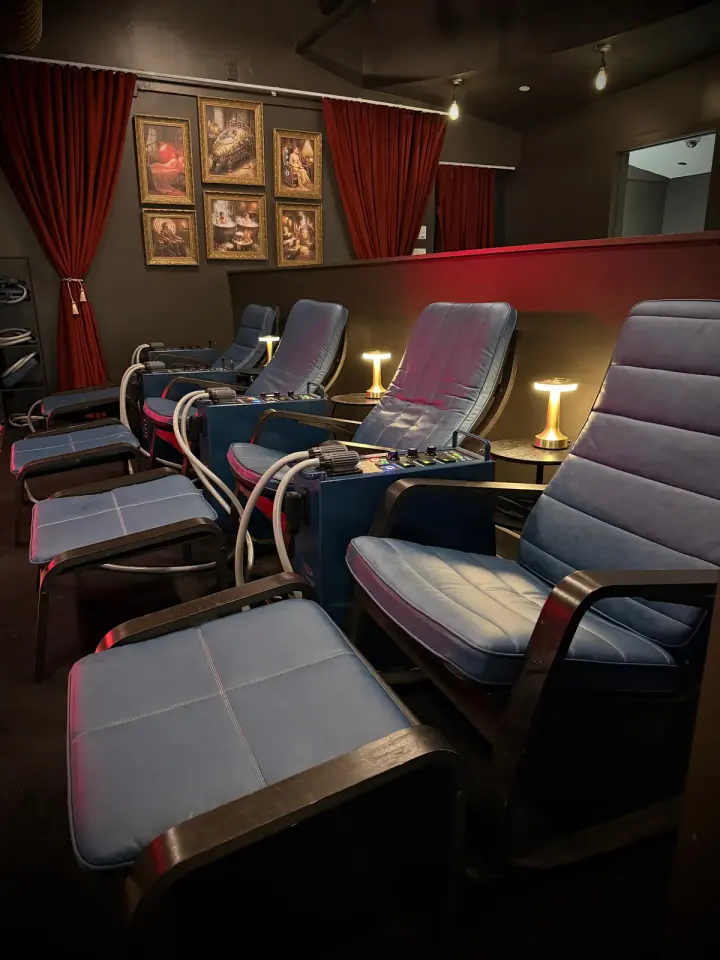 Row of blue recliners with framed artwork and red curtains in the recovery lounge at Healthspan
