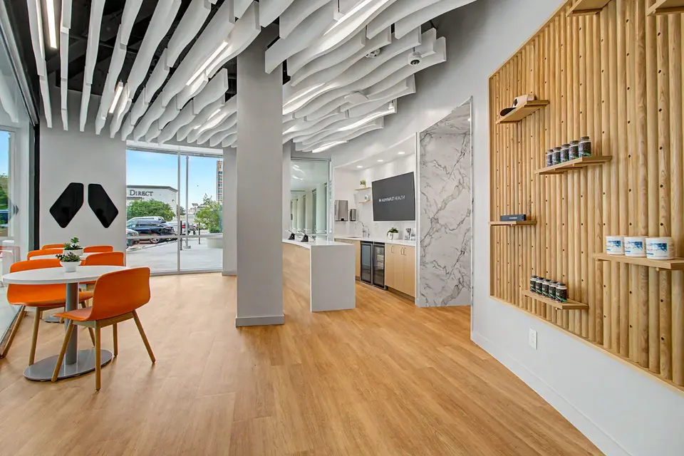 Member lounge at Humanaut Health Dallas with orange chairs, a slatted-wood product wall and curved ceiling baffles