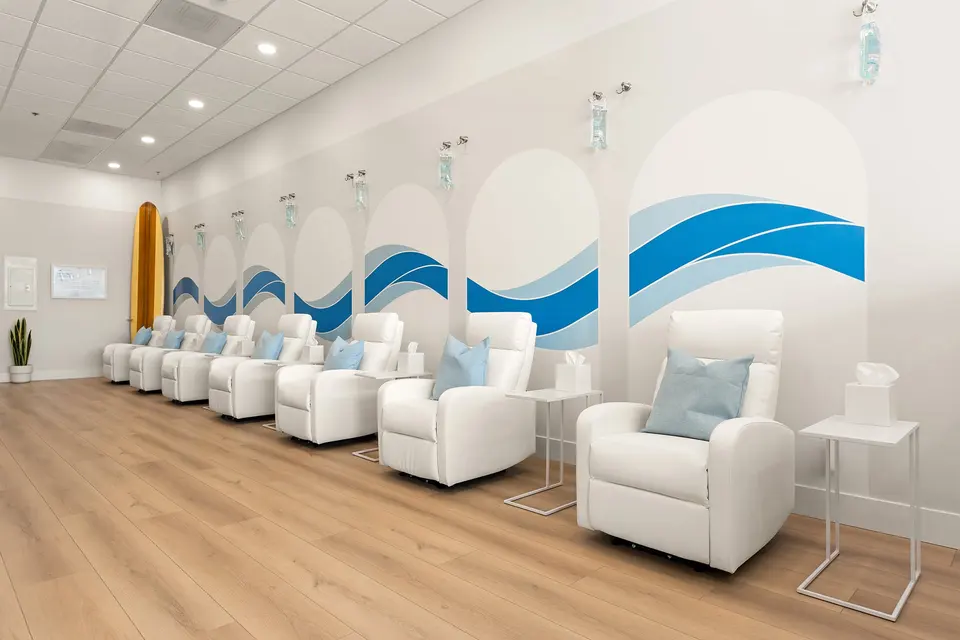 Row of white IV recliners under a blue wave mural at Hydration Room Manhattan Beach