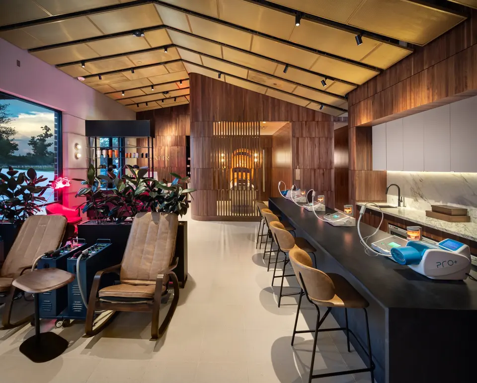 Interior of MATTR Bio Wellness Club with wood-slat walls, a long counter with recovery devices and lounge chairs by the window