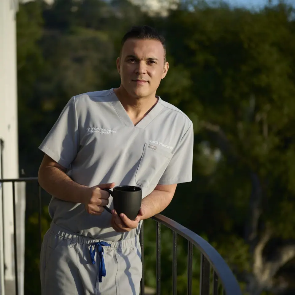 Dr. David Nazarian in scrubs holding a mug on a balcony