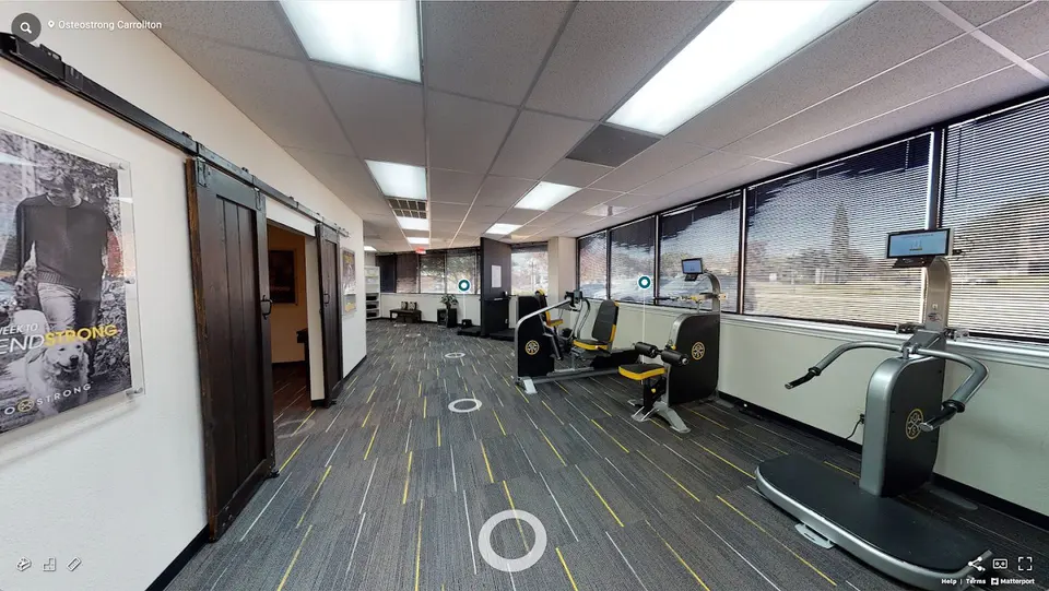 Session floor at OsteoStrong Carrollton with a row of OsteoStrong strength machines along a bank of windows