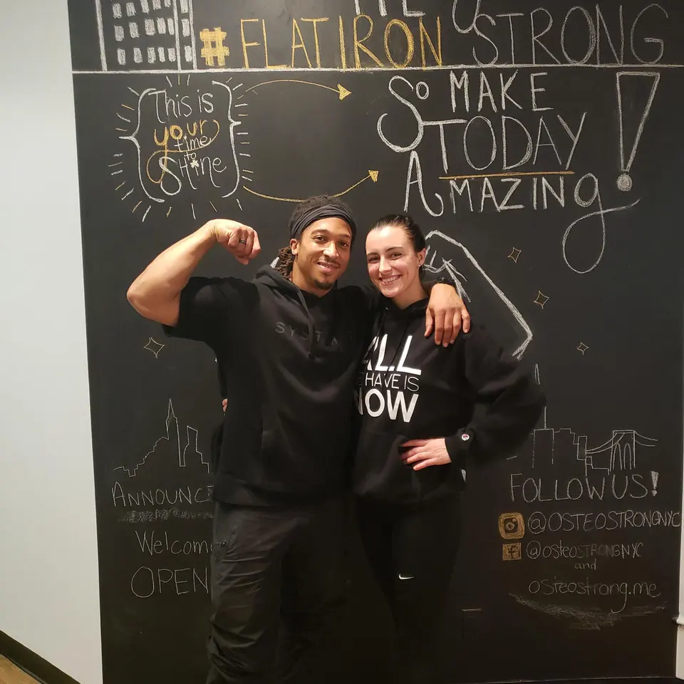 Two staff members posing in front of a '#FlatironStrong' chalkboard wall