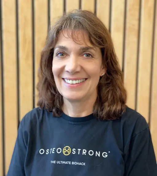 Portrait of owner Caryn Semelka in an OsteoStrong T-shirt in front of a wood-slat wall
