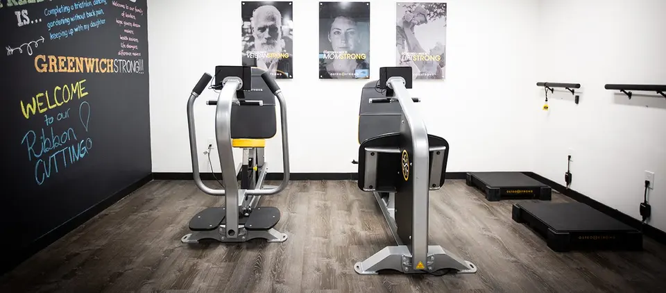 Two OsteoStrong machines beside a 'Greenwich Strong' welcome chalkboard