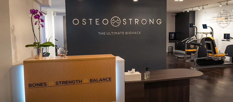 Reception desk with OsteoStrong wall sign and equipment area behind at OsteoStrong Upper West