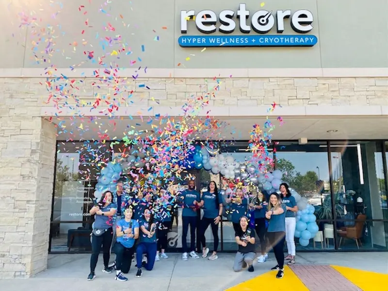 Restore Hyper Wellness Colleyville storefront with the team celebrating out front in a burst of confetti