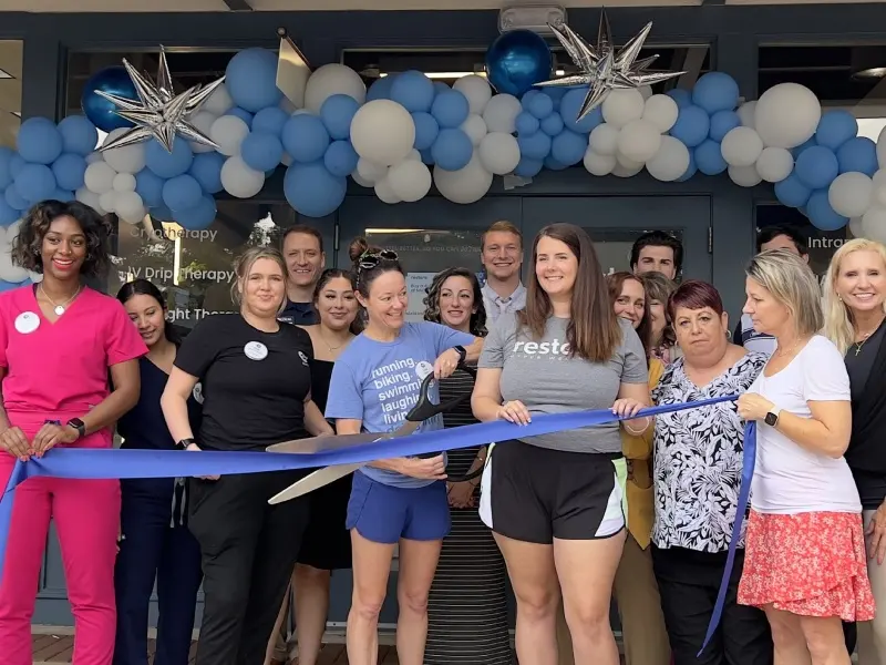 Restore Hyper Wellness Four Points staff at the ribbon cutting in front of the studio entrance, under a blue and white balloon arch