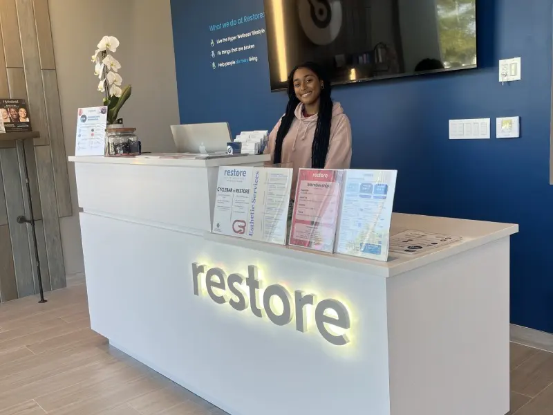 Staff member at the illuminated Restore reception desk in Pembroke Pines
