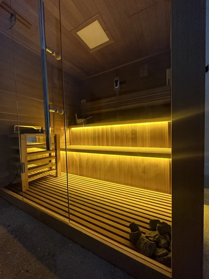 Glass-fronted wooden sauna with warm LED-lit benches at The Plunge & Sauna Method