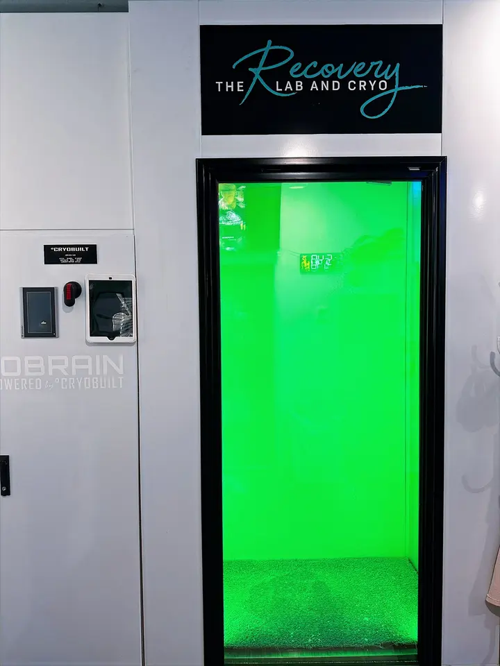 Cryotherapy chamber with a green-lit door under a The Recovery Lab and Cryo sign